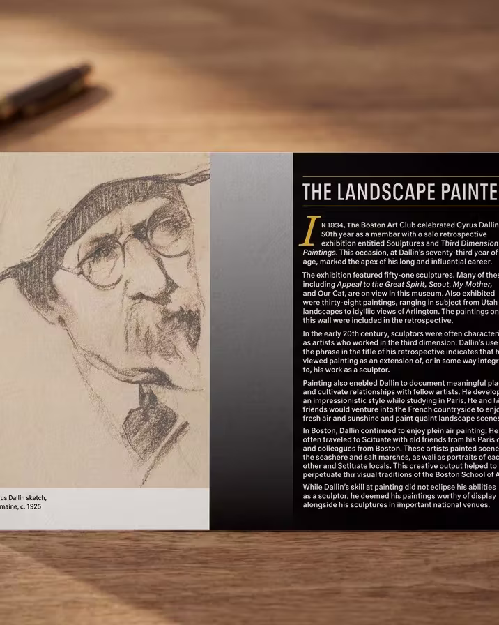 A Cyrus Dallin exhibition card, 'The Landscape Painter', lying on a desk beside a pen.